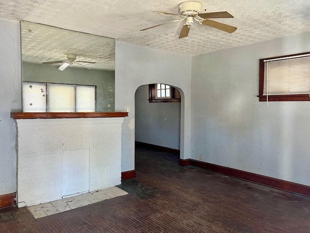 spare room with wood finished floors, baseboards, ceiling fan, a textured ceiling, and arched walkways