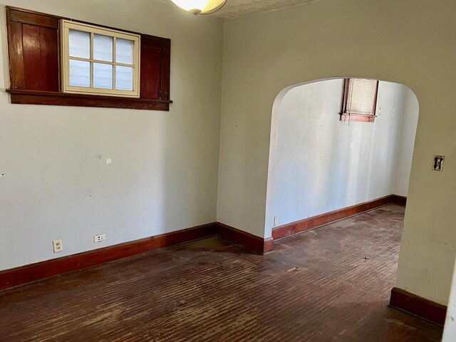 empty room featuring arched walkways, baseboards, and hardwood / wood-style flooring