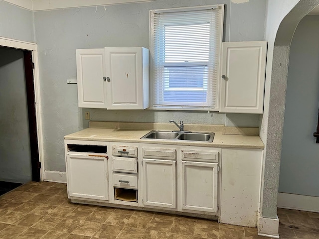 kitchen featuring arched walkways, a sink, baseboards, light countertops, and white cabinetry