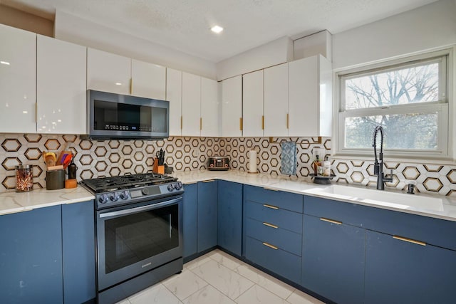 kitchen featuring appliances with stainless steel finishes, a sink, blue cabinetry, marble finish floor, and white cabinetry