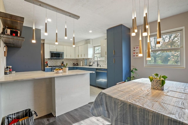 kitchen with a textured ceiling, appliances with stainless steel finishes, light wood-type flooring, light countertops, and a peninsula