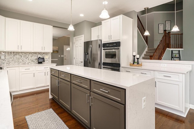kitchen with a center island, stainless steel appliances, white cabinetry, backsplash, and dark wood-style floors