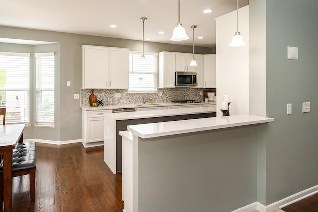 kitchen featuring dark wood-style flooring, baseboards, stainless steel microwave, white cabinets, and tasteful backsplash