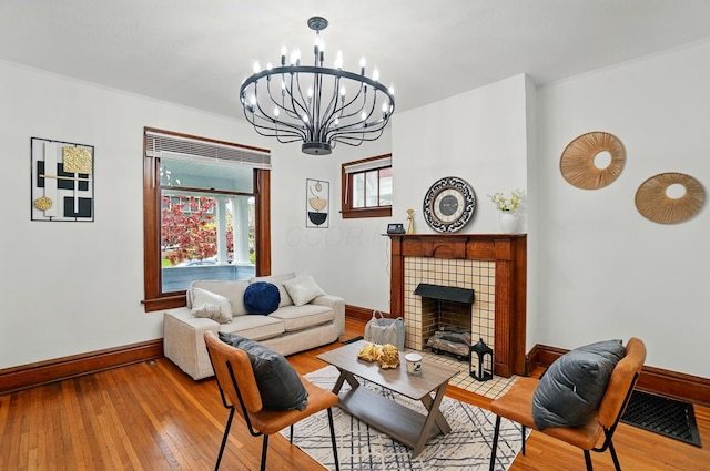 living area with visible vents, hardwood / wood-style floors, baseboards, a tiled fireplace, and a notable chandelier