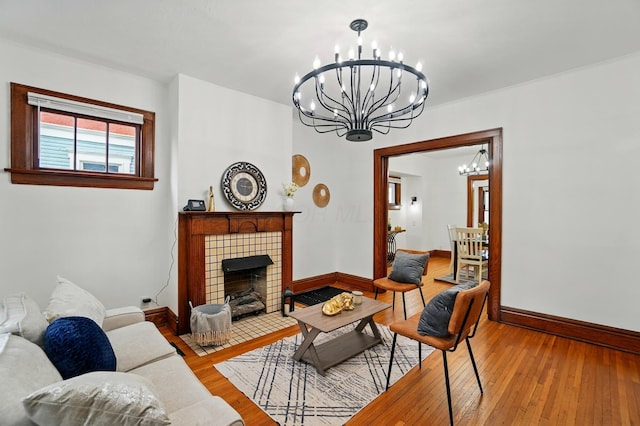 living room with wood-type flooring, baseboards, an inviting chandelier, and a tile fireplace