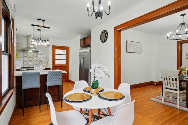 dining space with baseboards, light wood-style flooring, a notable chandelier, and a wealth of natural light