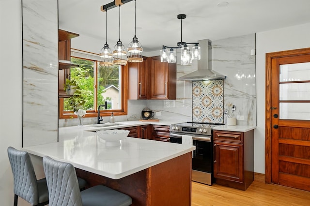 kitchen featuring wall chimney range hood, a kitchen breakfast bar, light wood-type flooring, stainless steel range with electric stovetop, and a sink