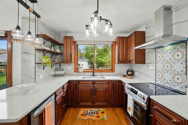 kitchen featuring wall chimney range hood, light wood-type flooring, a chandelier, a sink, and appliances with stainless steel finishes