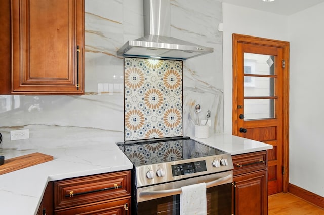 kitchen with electric range, wall chimney exhaust hood, backsplash, and light stone countertops