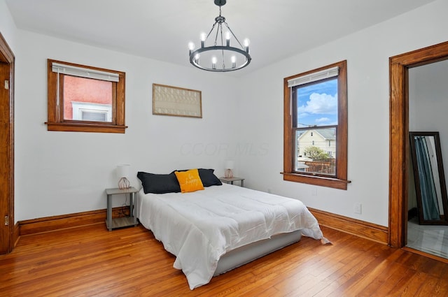 bedroom featuring an inviting chandelier, baseboards, multiple windows, and hardwood / wood-style flooring