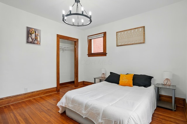 bedroom featuring an inviting chandelier, baseboards, a closet, and wood finished floors