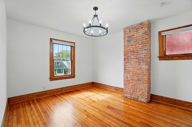 spare room featuring baseboards, wood-type flooring, and a chandelier