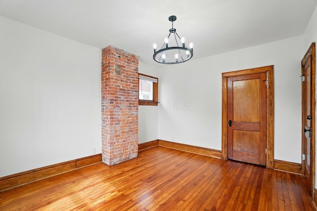 unfurnished room featuring wood-type flooring, baseboards, and a notable chandelier