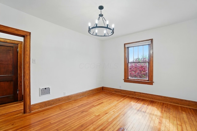 unfurnished room with an inviting chandelier, baseboards, light wood-type flooring, and visible vents