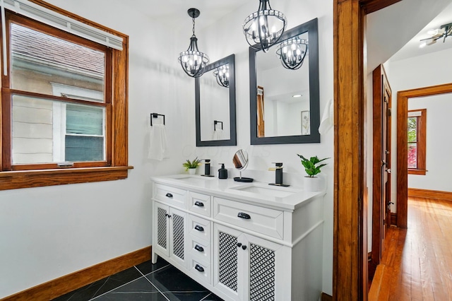 bathroom with a sink, baseboards, double vanity, and a chandelier