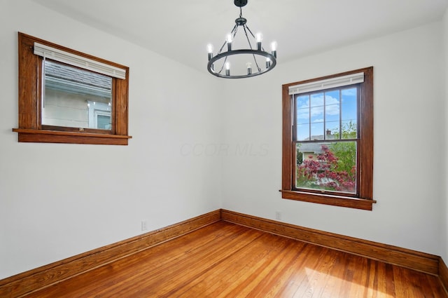 empty room with wood-type flooring, baseboards, and a notable chandelier