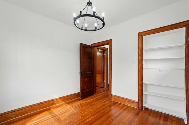 unfurnished bedroom with baseboards, a notable chandelier, and hardwood / wood-style floors