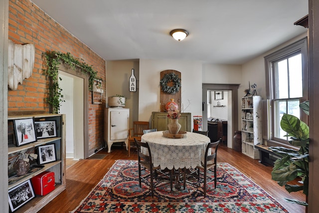 dining room featuring brick wall and dark wood-style floors