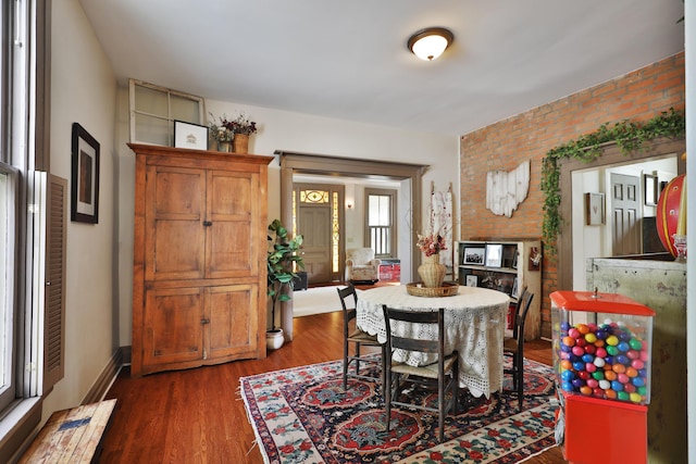dining room featuring brick wall and dark wood-type flooring
