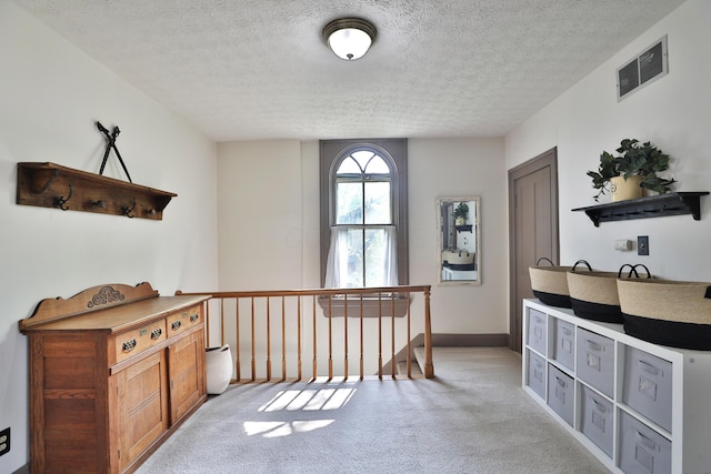 hallway featuring visible vents, a textured ceiling, an upstairs landing, and light colored carpet