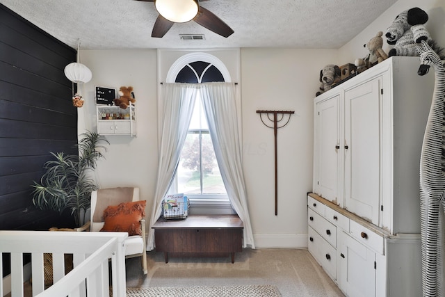 bedroom with ceiling fan, a textured ceiling, light colored carpet, visible vents, and baseboards