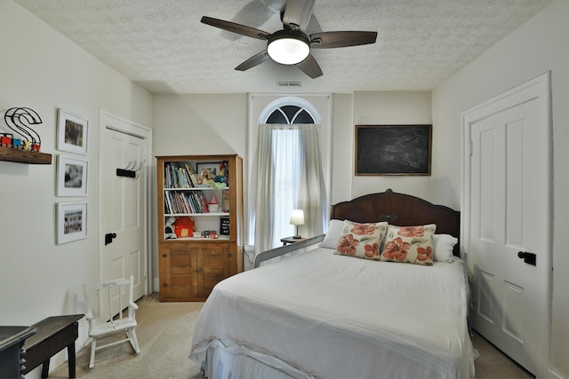 bedroom featuring a textured ceiling, visible vents, light carpet, and ceiling fan
