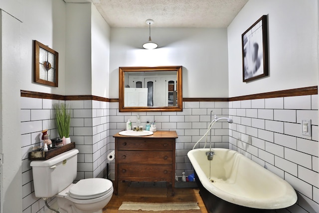 bathroom with tile walls, a soaking tub, vanity, and toilet