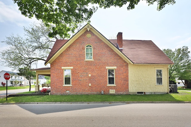 view of home's exterior with brick siding, roof with shingles, a yard, and a chimney