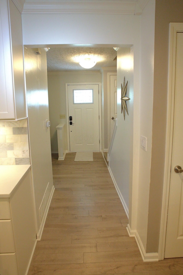 hall with light wood-style floors, baseboards, crown molding, and visible vents