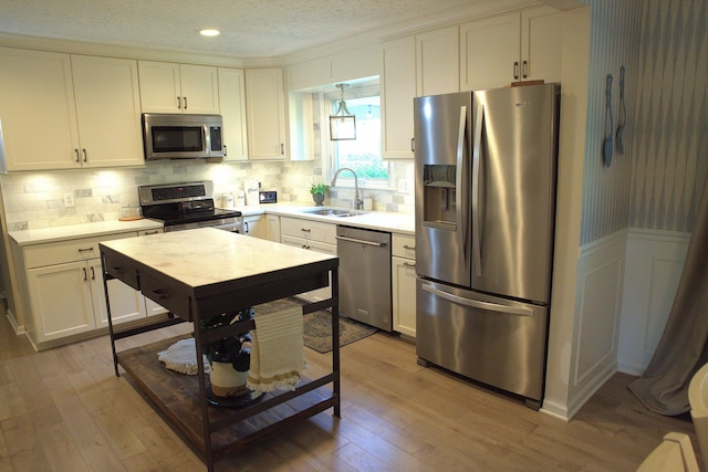 kitchen featuring light wood-style floors, light countertops, a textured ceiling, a sink, and stainless steel appliances