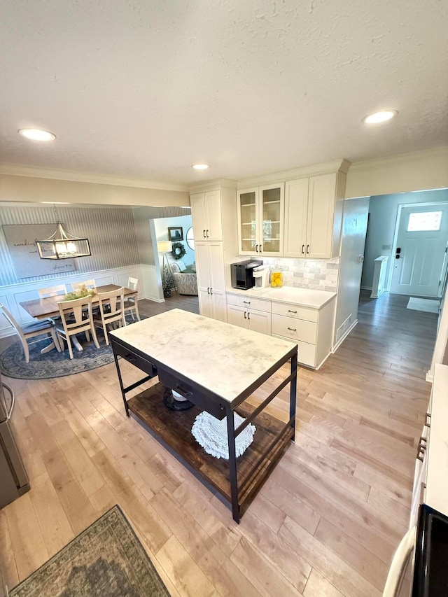 kitchen featuring decorative backsplash, light wood-type flooring, glass insert cabinets, ornamental molding, and white cabinetry