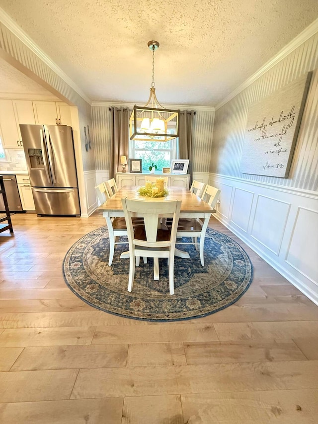 dining room featuring crown molding, a textured ceiling, an inviting chandelier, and light wood finished floors