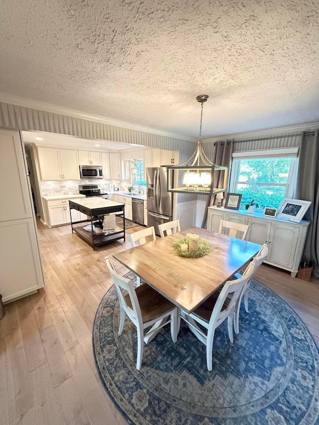 dining area with a textured ceiling, ornamental molding, and light wood-style flooring