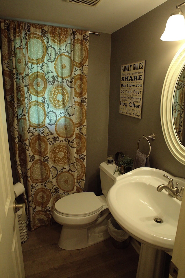 full bath with a shower with shower curtain, toilet, wood finished floors, and visible vents