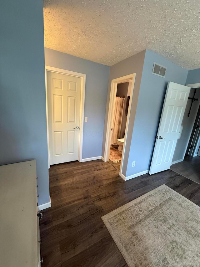 unfurnished bedroom featuring baseboards, dark wood-style flooring, a textured ceiling, and visible vents
