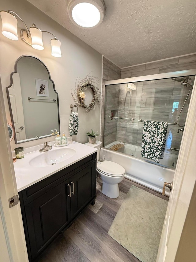 bathroom with vanity, toilet, a textured ceiling, enclosed tub / shower combo, and wood finished floors