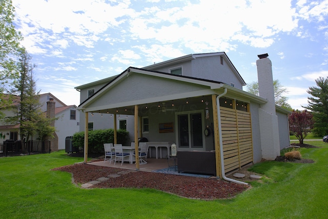 back of house featuring a lawn, a chimney, and a patio area