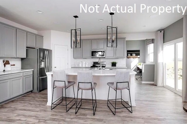 kitchen with gray cabinets, a sink, stainless steel appliances, light wood-style flooring, and an island with sink