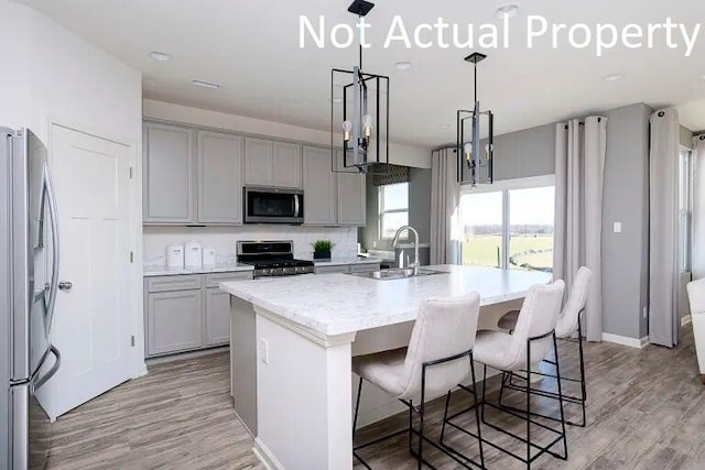kitchen featuring a sink, gray cabinets, appliances with stainless steel finishes, and a center island with sink