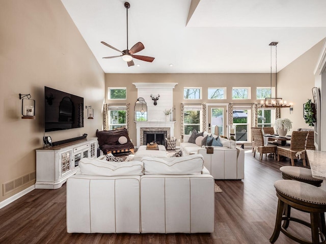 living area with a fireplace, high vaulted ceiling, ceiling fan with notable chandelier, visible vents, and dark wood-style floors