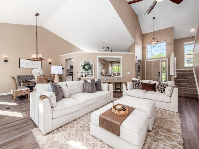 living room with high vaulted ceiling, ceiling fan with notable chandelier, baseboards, wood finished floors, and stairway