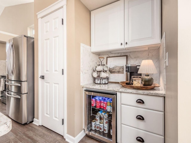 bar with beverage cooler, freestanding refrigerator, baseboards, tasteful backsplash, and a bar
