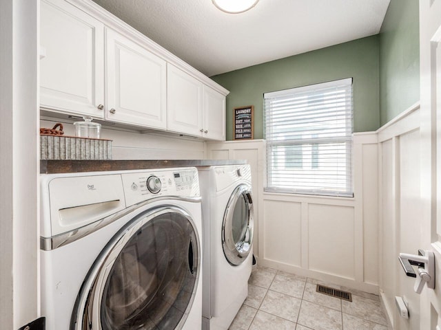 washroom with visible vents, a decorative wall, washer and dryer, cabinet space, and light tile patterned floors