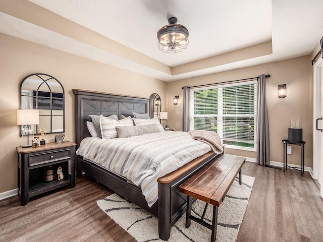 bedroom featuring baseboards, a notable chandelier, wood finished floors, and a raised ceiling