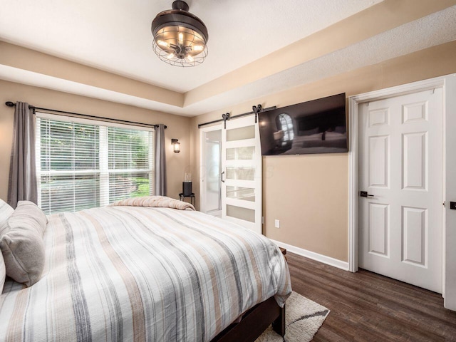 bedroom featuring baseboards, dark wood finished floors, a barn door, and a chandelier