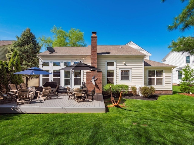 back of property featuring a lawn, a deck, a chimney, and roof with shingles