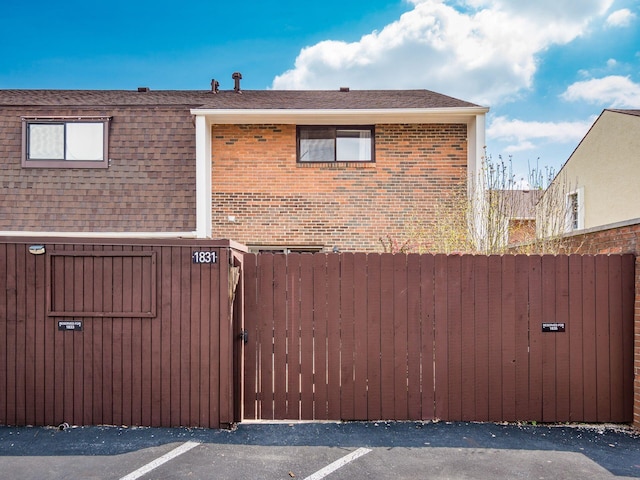 view of property exterior featuring brick siding, a gate, roof with shingles, and fence