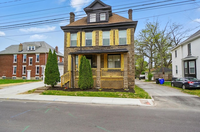 traditional style home with covered porch, a chimney, and stone siding