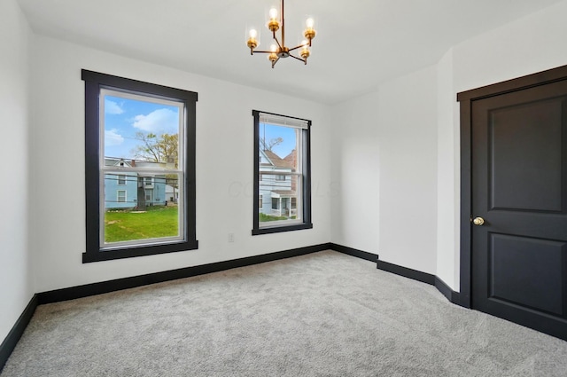 carpeted empty room featuring baseboards and a chandelier