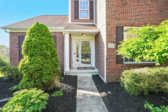 doorway to property with roof with shingles and brick siding